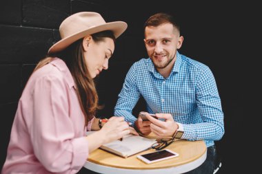 Portre pozitif genç adam ise kameraya gülümseyen ve rekreasyon vaktinizi kahvehane iç kız arkadaşı ile 4 g internet bağlantısı kullanarak modern smartphone uygulama güncelleştiriliyor