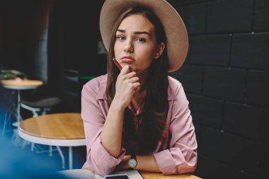 Genç kadın şık şapkalı kahve masada oturan yarım uzunluk portre. Kafeteryada istirahat ederken kameraya el arıyorum kalem ile mutsuz hippi kız. Kötü ruh ile sevimli kadın blogger