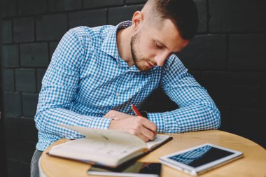 Dalgın akıllı hipster öğrenci kafede kahve masada oturan Not Defteri'nde metin aşağı yazma. Ödev not defterindeki kroki çizim yetenekli genç adam. Erkek blogger notları yayın yapma