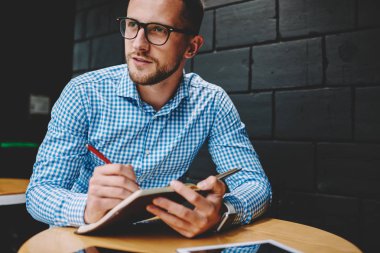 Düşünceli yakışıklı genç şık Eyewear uzağa bakarken Not Defteri'nde aşağı yazma. Hipster adam çizim kroki üzerinde geliştirme kendi iş için yeni yaratıcı fikirler düşünürken durulması