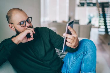 Web sayfası üzerinden dijital tablet, ciddi üzerinde rezervasyon yaparken düşünme gözlük dalgın beyaz adam online ücretsiz zaman rahat evinde geçirmek bilgi okuma hipster adam sakallı