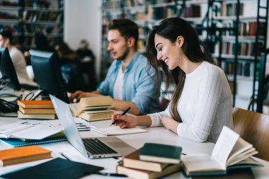 Kız öğrencinin yazılı ödev erkek arkadaşı, edebiyat ve modern technolog kullanarak araştırma yapma college Kampüsü zaman harcama olumlu genç kadın yakın oturan Üniversitesi Kütüphanesi olarak gülümseyen