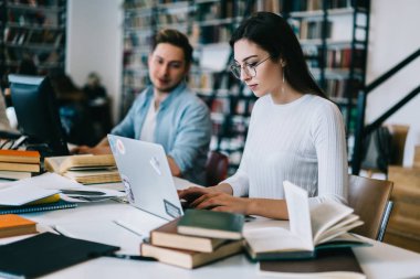 Kız öğrenci ödev olarak modern üniversite kütüphanesi Wi-Fi, Genç kadın ve erkek birlikte technolog kullanarak üniversite kampüsünde eğitim için dizüstü bilgisayar oluşturma raporu yazmaya konsantre
