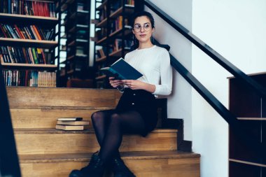 Üniversite Kampüsü, zeki güzel kız öğrenci Otodidakt edebiyat sırasında ücretsiz tim ilginç zevk zaman harcama merdivenlerde kitap ile oturan Eyewear çekici genç kadın