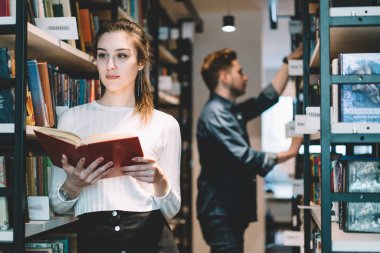Ciddi bayan üniversite öğrencisi de rahat kıyafet edebiyat ayakta raflardan mağaza, iş holding kitap sipariş librar içinde yapım konsantre çekici genç kadın kütüphaneci yakınındaki üzerinde durulması
