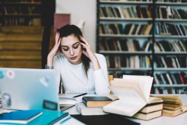 Dizüstü bilgisayar ve kitap, üzgün kız öğrencinin kafası elinde tutan ağrıdığı kampüsünde okurken kullanarak kurs proje oluşturmak için mutsuz genç kadın duygu ağrı overworked