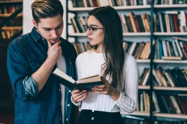 Kadın ve erkek öğrencilerin ders kitabı birlikte okuma konsantre bilgi analiz, zeki genç kadın ve ilginç yeni harcama hakkında konuşan adam zaman eğitim Üniversitesi librar