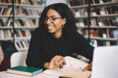 Tamamlanan çalışma ile laptop vasıl okul sırası, koyu tenli kadın ise araştırma yapma ve netboo kampüste öğrenme gülüyor oturan yaratıcı Afrikalı-Amerikalı kadın serbest tasarımcı memnun