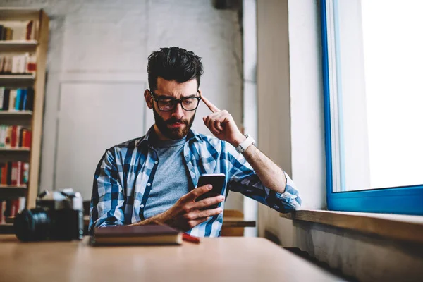 年轻的困惑时髦的家伙在眼镜阅读文本信息从工作中使用手机上的应用 集中男性博客下载文件的现代智能手机连接到 Wifi — 图库照片
