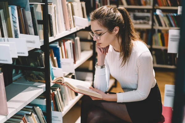 Pensive Female Student Eyewear Vision Protection Sitting Bookshelves Reading Interesting — Stock Photo, Image