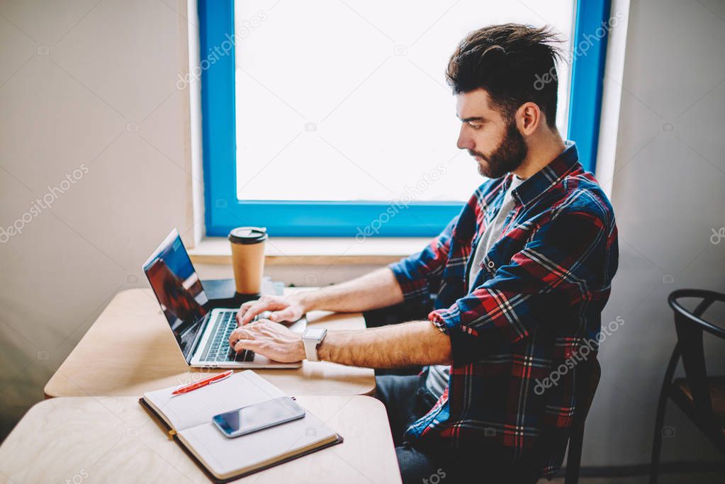 Young millennial male using laptop computer and watching webinar for get knowledge from e learning, skilled clever student reading information and browsing internet via netbook in coworking space