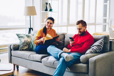 Hipster çift birlikte kitap okuma ve smartphone kullanımını serbest zaman harcama, kablosuz bağlantı, posta cellula üzerinde kontrol adam kullanarak yeni daire genç evlilik memnun