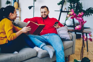Romantik Çift yeni kitabı ücretsiz birlikte rahat ev iç, mariggecommunicating üzerinde boş zaman, hipster adam holding smartphone olumlu kız arkadaşıyla konuşurken vakit tartışırken gülümseyen