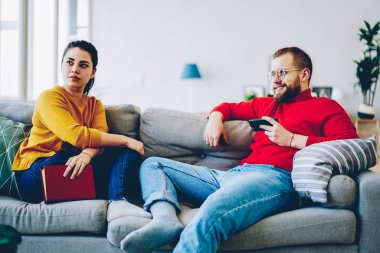 Genç yenilikçi ve rahat ev iç, adam kitap onun kız arkadaşı ise cep telefonu için kablosuz bağlantı kullanarak, birlikte vakit kanepede oturan ilişkide erkek