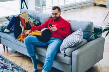Genç kadın ilginç kitap sosyal ağlar, Romantik Çift rahat ev iç huzur zevk yeni veri kaynağı denetimi için cep telefonuyla erkek koltukta yalan