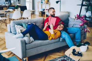 Kaç aşk harcama boş zaman evde içinde kadının edebiyat sevgilisi sosyal ağlar üzerinden smartphone kanepede haberlerde kontrol ederken ilginç bir kitap ve modern gadget, dinlenme