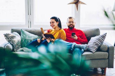 Neşeli hippi kız erkek arkadaşının şaka ücretsiz rahat evinde birlikte, vakit pozitif kadın kocası smartphone kullanımını kitabı okuma gülüyor 