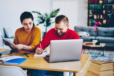 Kadın ve erkek meslektaşları netbook, masaüstü belgeleri okuma ve birlikte bilişim tartışırken bazı notlar yazma, oturan genç aile kullanarak belgeleri kontrol birlikte proje üzerinde işbirliği