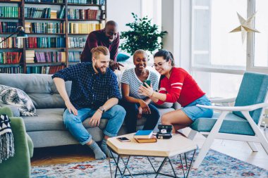 Komik videolar sosyal ağlardan üstünde hareket eden telefon, gülüyor arkadaşlar komik fotoğraflar smartphone dinlenme ile ilgilenen erkek ve dişi hipsters gülümseyen neşeli çok ırklı Grup 