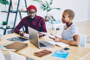 Kağıtları ve belgeleri vasıl okul sırası kontrol ciddi Afro-Amerikan erkek ve kadın iş arkadaşları, zeki karanlık alan togethe coworking dizüstü bilgisayar kullanan proje üzerinde işbirliği ortakları derili.
