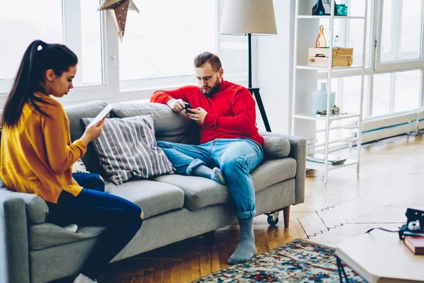 Young couple spending time at home ignore real communication  chatting in social networks via smartphone and wifi connection, millennial male and female hipsters