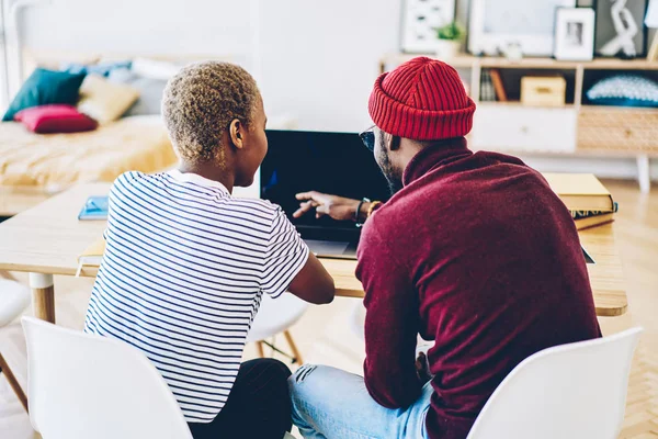 Back view of african american couple watching video on laptop computer sitting at apartment,dark skinned male and female browse web page on netbook making online shopping together at home interio