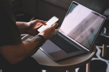 Adamın elleri 4 g kullanarak dijital Smartphone cep telefonu ile sosyal ağlarda profil güncelleştirme görünümünü kırpılmış Internet dizüstü cihaz oturuyor. Holding telefon ve app üzerinde dijital hücresel yükleme genç adam