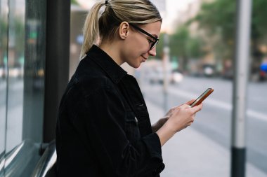 Online sosyal ağlar 4 g kullanarak modern smartphone cep telefonu ile sohbet ederken gülüyor neşeli genç kadın blogger yan görünüm Internet. Hücresel tutarak ve haber web sitesinde okumak pozitif hippi kız