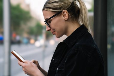Yan görünüm pozitif hippi kız blog Smartphone cep telefonu ile takipçileri ile sohbet ederken gülüyor. Gözlük dijital cep telefonu 4 g kullanarak Web sitenizde video izlerken neşeli genç kadın Internet