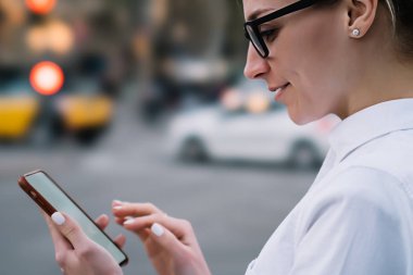 Hipster blogger el ve okuma gelen bildirim iyi haber ile modern smartphone holding gözlük gülümseyen kırpılmış yan görünüm. Online video izlerken gülmekten olumlu genç kadın
