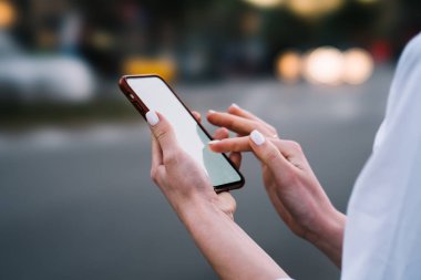Kadının elleri ile modern smartphone aygıt boş ekranda parmak metin iletisi yazmaya ve kentsel ayarı bulanık arka plan üzerinde sosyal ağlarda arkadaşlarınızla sohbet online görünümünü kırpılmış