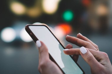 Boş ekranda bokeh arka plan üzerinde modern akıllı telefon kısa mesaj yazarak parmaklar görünümünü kırpılmış. Hareket eden telefon tutarak ve sohbet online sosyal ağlar kadının elleri