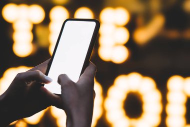 Akıllı telefon elinde tutan ve modern cihazın arka plan ile gece ışık ve aydınlatma üzerinde Internet bağlantısı kullanarak boş ekranda metin parmak ile yazarak kadının el görünümünü kırpılmış
