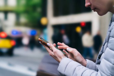 Smartphone aygıt tutarak ve 4 g internet bağlantısı üzerinde arka plan bulanık kullanarak aygıt üzerindeki parmak ile yazarak genç kadın yan görünüm kırpılmış. Sohbet online dijital hücresel hipster blogger