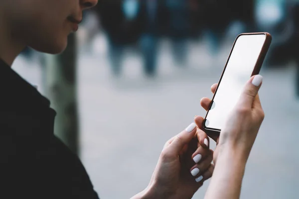 Cropped view of young woman holding smartphone with blank screen area for your internet website.Hipster blogger with mobile phone in hands updating app on gadget with mock up area for web page