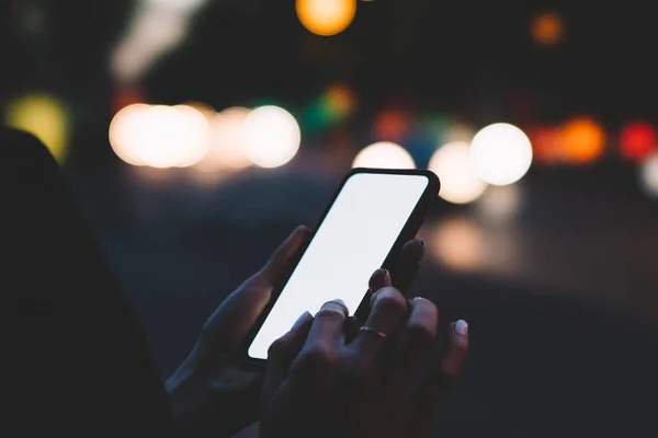 在散景的背景下使用4G 互联网的年轻女子手持现代智能手机在夜间灯光下观看 带空白屏幕区域的数字手机广告短信 — 图库照片