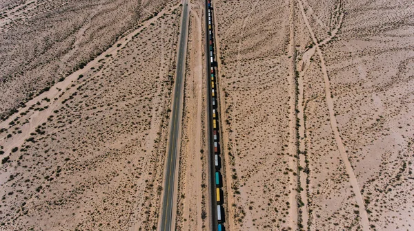Aerial view of train containers shipping goods in wild environment, locomotive freight on railroad transporting cargo through desert lands in Arizona. Logistic and delivery shipping goods everywhere