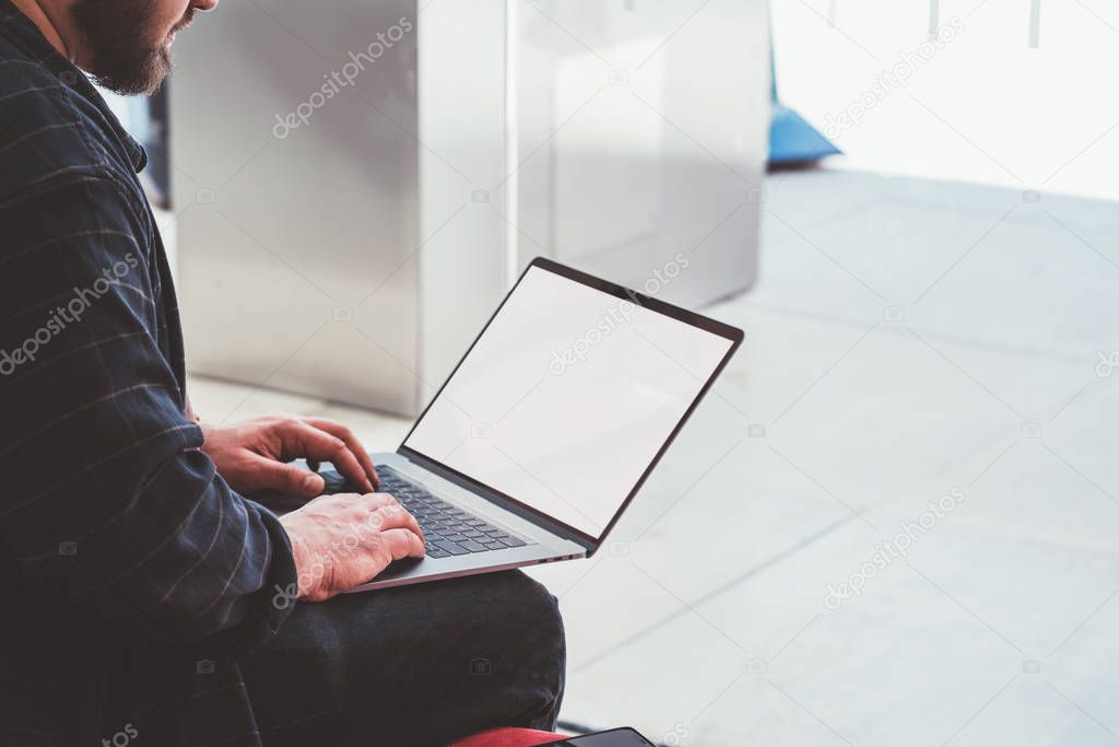 Cropped view of young man in casual wear typing text information on modern laptop with blank screen area for your internet content.Male freelancer working remotely at computer with mock up