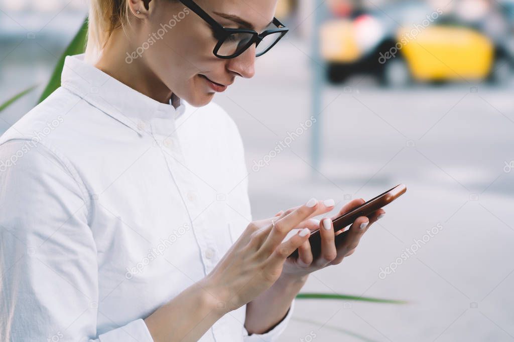 Cropped view of young woman blogger dressed in casual wear holding smartphone in hand and typing with finger on device chatting online.Hipster girl updating app on mobile phone using 4G internet