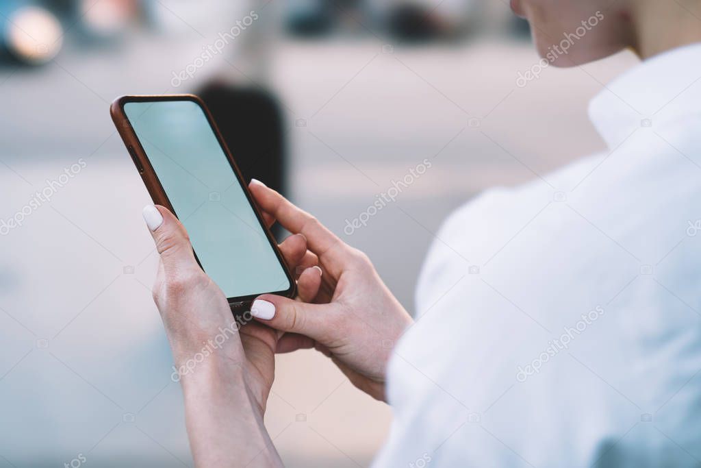 Cropped view of woman's hand holding modern smartphone with blank screen area for your internet website.Hipster female blogger updating profile in social networks on mobile phone device