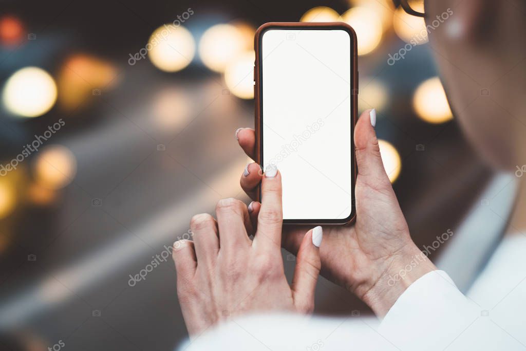 Cropped view of woman's hands holding smartphone and touching with finger on blank display of gadget to install app using internet.Cellular with copy space area for your web page on bokeh background