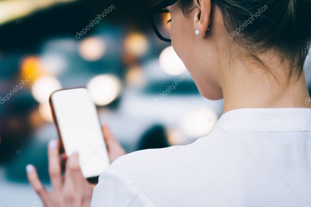 Cropped back view young woman holding smartphone and installing app on gadget using free 4G internet on bokeh background.Hipster girl making transaction online on website on digital telephone