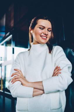 İç yüzünde, sevimli gülümseme ile aşağı bakıyor ve arkadaş Üniversitesi Kampüsü bekleyen trendy giyim gülümseyen pozitif hipster kız ayakta beyaz süveterli neşeli beyaz kız öğrenci