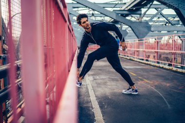 Trendy eşofman başlamadan önce elektronik kulaklık üzerinden dinleme radyo sırasında açık havada egzersiz yapıyor sokak, Genç jogger genelinde çalışan şehir Köprüsü üzerinde uzanan yakışıklı Avrupa sporcu