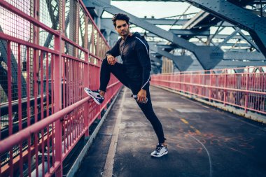 Yakışıklı esmer saç runner dinlenme sırasında kulaklık müzik dinlerken eğitim alarak siyah spor kıyafeti. Mola egzersiz yaptıktan sonra şehirde öğleden sonra genç erkek koşucu