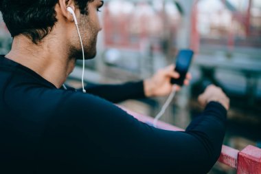 Arkadan görünüşü eğitim havada küçük mola verme ve motivasyon, aktif erkek atlet elektronik kulaklık ve mobil uygulama üzerinden müzik dinleme için yeni şarkılar arama genç sporcu