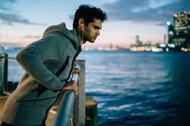 Erkek koşucu korkuluk Nehri yakınında esneklik akşam hakkında dinleme ses yönergeleri sırasında gece şehir genelinde koşu sonra dinlenme egzersizleri, ciddi sporcu sağlıklı yaşam üzerinde durulması