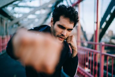 Erkek bulanık cephe süsleme, ciddi Avrupa sporcu mücadele spor kameraya seyir sırasında kentsel ayarı uygulamak ve güç yumruk yaparak eşofman içinde yarım uzunluk portre yumruk sıkılı