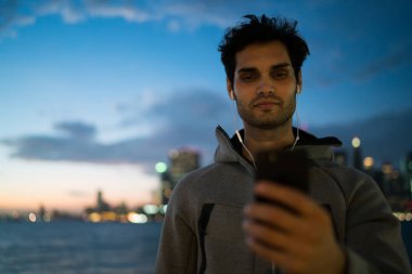 Etkin atletik sporcu kardiyo tatilinde mobil uygulama aracılığıyla metin mesajları okuma, açık havada, telefonda sohbet ve akşam koşu sonra müzik keyfi Avrupa erkek koşucu egzersizleri