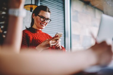 Sosyal ağlarda profil güncelleştirme neşeli hippi kız bağlı kablosuz 4 g için kapalı, eğlence genç gülümseyen kadın komik video telefonda app kullanarak izlerken Eyewear dinlenme internet